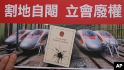 FILE - An activist holds a card at a protest near the West Kowloon terminus of the Guangzhou-Shenzhen-Hong Kong Express Rail Link, Dec. 28, 2017. Some Hong Kong legal scholars say the "co-location arrangement," location where mainland customs and immigration officers from China will be stationed, is unconstitutional as it contravenes the city's Basic Law and "one country, two systems" way of governing Hong Kong.