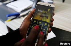 FILE - A customer uses her cell-phone to access the Sidian Bank mobile-app inside the banking hall at the Sidian Bank headquarters on the outskirts of Kenya's capital Nairobi.