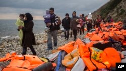 FILE - Refugees and migrants walk along a beach after crossing a part of the Aegean on a dinghy, from Turkey to the Greek island of Lesbos, Dec. 12, 2015. 