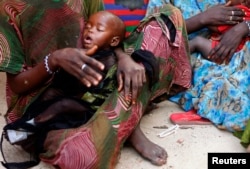 FILE - A woman holds her malnourished child in Sirlaabe IDP camp in Mogadishu, Somalia, June 28, 2012.