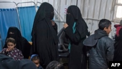 Two women (C), reportedly wives of Islamic State (IS) group fighters, wait with other women and children at a makeshift clinic at the Internally Displaced Persons (IDP) camp of al-Hol in al-Hasakeh governorate in northeastern Syria, Feb. 7, 2019. 