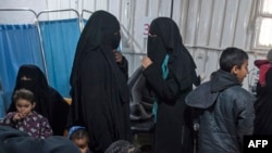 FILE - Two women, reportedly wives of IS fighters, wait with others in the internally displaced persons camp of al-Hol in al-Hasakeh governorate, Syria, Feb. 7, 2019. The United States is refusing to take back a U.S.-born IS propagandist, saying she is no longer a citizen.
