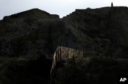 FILE - In this June 22, 2016, file photo, light illuminates a section of the primary fence separating Tijuana, Mexico and San Diego, in San Diego.