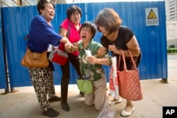 Bao Lanfang, second from right, whose daughter-in-law, son and granddaughter were aboard Malaysia Airlines Flight 370, kneels in grief while speaking to journalists outside the company's offices in Beijing, Aug. 6, 2015.