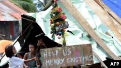 Children around a makeshift shelter beside a message on a board, next to a Christmas tree on a street in Basay, Samar province, Nov. 28, 2013.