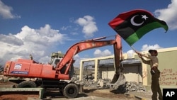 A boy waves a Kingdom of Libya flag as a bulldozer demolishes walls of the residence of Moammar Gadhafi at the Bab al-Aziziyah complex in Tripoli, October 16, 2011.