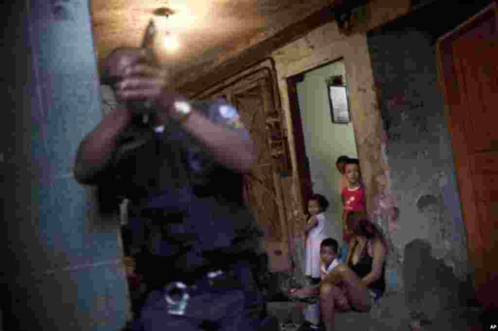 Residents stand at the entrance of a house as a police officer takes position during an operation at Rocinha slum in Rio de Janeiro, Brazil, Friday April 6, 2012. Hundreds of police from different units are still searching for the man who killed a police