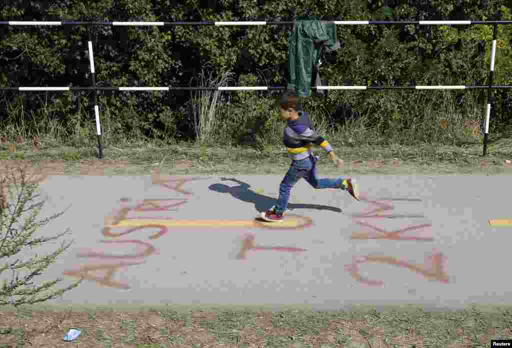 A boy jumps over a sign marking the distance to the Austrian border as migrants leave Hegyeshalom, Hungary.