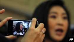 A woman uses her mobile phone to take a picture of Prime Minister-elect Yingluck Shinawatra as she addresses reporters at her party's headquarters in Bangkok, July 13, 2011.