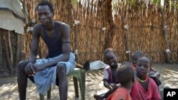 FILE - A South Sudanese man, who says he was shot in the back and thigh by government soldiers while trying to get food in a nearby town in order to feed his starving family, sits with his five children outside his house in Jiech, Ayod County, South Sudan