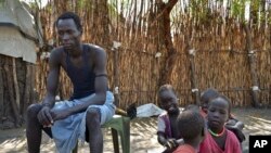 FILE - A South Sudanese man, who says he was shot in the back and thigh by government soldiers while trying to get food in a nearby town in order to feed his starving family, sits with his five children outside his house in Jiech, Ayod County, South Sudan.