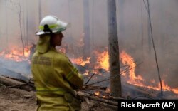 A firefighter keeps an eye on a controlled fire as they work at building a containment line at a wildfire near Bodalla, Australia, Sunday, Jan. 12, 2020.