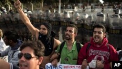 Barisan polisi anti huru-hara berdiri di belakang para demonstran yang meneriakkan slogan anti kekerasan di luar stadion Minerao, di kota Belo Horizonte, Brazil, saat berlangsungnya pertandingan sepakbola antara tim Jepang melawan Meksiko, Sabtu (22/6).