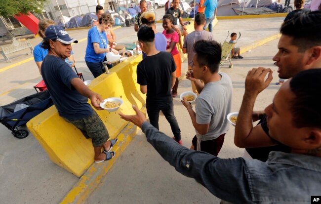 FILE - Migrants seeking asylum in the United States receive breakfast from a group of volunteers near the international bridge, April 30, 2019, in Matamoros, Mexico.