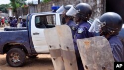 Liberian policemen, right, dressed in riot gear disperse a crowd of people that blocked a main road after the body of someone suspected of dying from the Ebola virus was not removed by health workers in the city of Monrovia, Liberia, Aug. 14, 2014. 