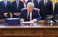 FILE - U.S. President Donald Trump signs the $2.2 trillion coronavirus aid package bill as he sits at the Resolute Desk in the Oval Office of the White House in Washington, March 27, 2020.