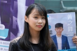 In this Sept. 28, 2019, photo, Hong Kong pro-democracy activist Agnes Chow stands next to a poster of activist Joshua Wong, in Hong Kong.