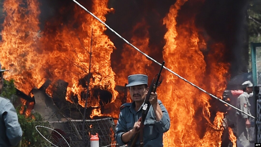 An Afghan policeman stands guard as smoke and flames rise from the site of a huge blast struck near the entrance of Kabul's international airport, in Kabul on August 10, 2015. 