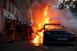 Fire-fighters pull off a fire on a burning car during a demonstration against a security law that would restrict sharing images of police, Nov. 28, 2020 in Paris.