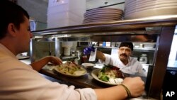 FILE - Cook Bulmaro Sosa, right, goes over a food order with server Zachary DeYoung at an Ivar's restaurant in Seattle.