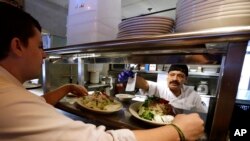 FILE - Cook Bulmaro Sosa, right, goes over a food order with server Zachary DeYoung at an Ivar's restaurant in Seattle.