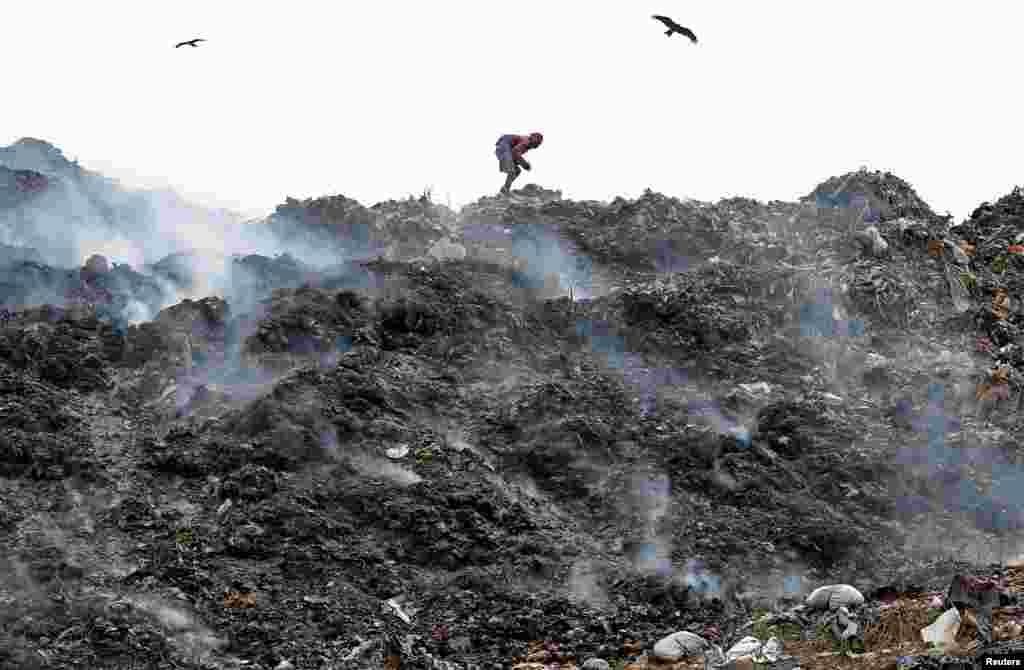A man collects recyclable materials as smoke billows from a burning garbage dump site in Kolkata, India.