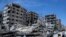 FILE - People stand in front of damaged buildings, in the town of Douma, the site of a suspected chemical weapon attack, near Damascus, Syria, on April 16, 2018. 