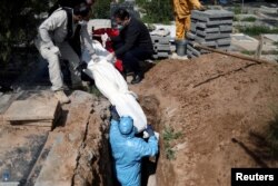 FILE - Iranian men bury journalist Abdollah Zavieh, who died of COVID-19, at Behesht Zahra cemetery in Tehran, March 24, 2020.