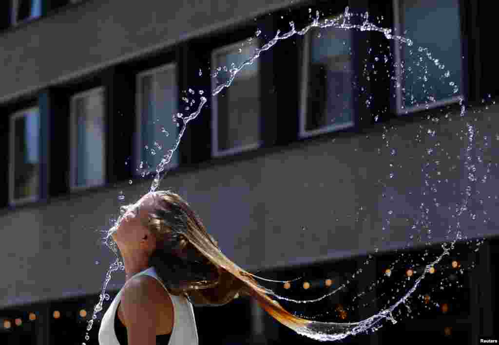 A woman swings her hair back after dipping her head into a fountain in Budapest, Hungary July 6, 2015. Over the weekend, a heat wave has reached Hungary with temperatures topping 38 degrees Celsius (100.4 degrees Fahrenheit). REUTERS/Laszlo Balogh - RTX1J