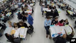 FILE - Workers at the Broward County Supervisor of Elections office, foreground, show Republican and Democrat observers ballots during a hand recount in Lauderhill, Fla., Nov. 16, 2018. 