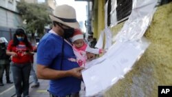 A man holding his infant daughter checks a voting list in the elections to choose members of the National Assembly, in Caracas, Venezuela, Dec. 6, 2020.