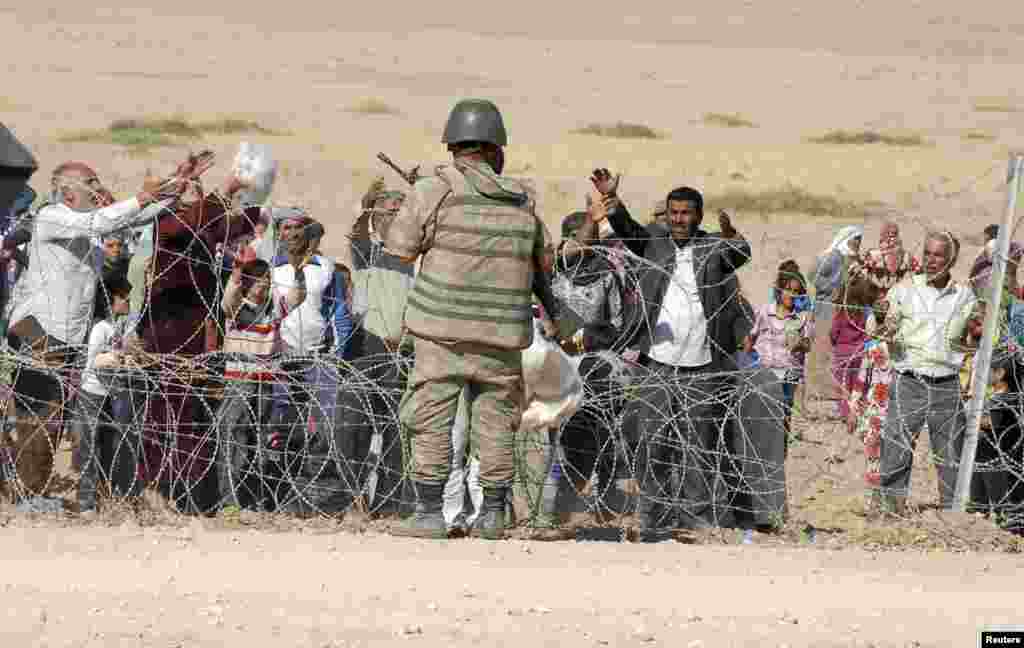 A Turkish soldier stands guard as Syrian Kurds wait behind the border fence to cross into Turkey near the southeastern town of Suruc in Sanliurfa province, September 19, 2014. Several thousand Syrian Kurds began crossing into Turkey on Friday fleeing Isla