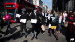 FILE - Men dressed as 1920s newspaper boys with ‘greyscale’ make up pose for photographs as they hand out specially made newspapers that feature two chapters of the latest novel featuring fictional Belgian detective Hercule Poirot outside Oxford Circus underground train station in London, May 21, 2015.