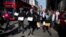 FILE - Men dressed as 1920s newspaper boys with ‘greyscale’ make up pose for photographs as they hand out specially made newspapers that feature two chapters of the latest novel featuring fictional Belgian detective Hercule Poirot outside Oxford Circus underground train station in London, May 21, 2015.