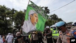 Pendukung Rizieq Shihab, pemimpin Front Pembela Islam (FPI), mengibarkan bendera dengan gambarnya saat unjuk rasa di Jakarta, Jumat, 18 Desember 2020.
