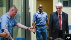 Former Bosnian Serb leader Radovan Karadzic, right, is shown his seat as he arrives to open his appeal at a U.N. court against his convictions on charges including genocide and crimes against humanity and his 40-year prison sentence in The Hague, Netherlands, April 23, 2018.