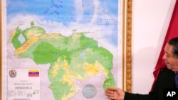 Ketua dari Komite Khusus untuk Pertahanan Wilayah Guyana Essequibo, Herman Escarra, berdiri di samping peta baru Venezuela yang mencakup wilayah sengketa Essequibo, dalam acara pengumuman peta baru itu di Caracas, Venezuela, pada 8 Desember 2023. (Foto: AP/Matias Delacroix)