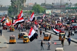 Demonstrators hold national flags as they head toward Tahrir Square for anti-government protests in Baghdad, Iraq, Oct, 1, 2020.