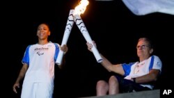 Brazilian judo gold medalist Rafaela Silva, left, and Tomas Magalhaes, member of the Archdiocese of Rio de Janeiro, carry Paralympic torches in front of the Christ the Redeemer statue on its way for the opening ceremony in Rio de Janeiro, Brazil, Tuesday,