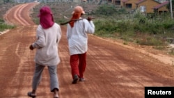 FILE - Women walk past houses, built for the residents being displaced by land sales, at Botum Sakor National Park in Koh Kong province, Feb. 20, 2012. About 200 families displaced by construction have returned to their homes, demanding more compensation.