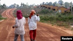 FILE - Women walk past houses, built for the residents being displaced by land sales, at Botum Sakor National Park in Koh Kong province, Feb. 20, 2012.