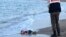 FILE - A Turkish police officer observes the body of migrant child Aylan Shenu on the beach at Bodrum, southern Turkey. Syrians Muwafaka Alabash and Asem Alfrhad were convicted of human trafficking in the deaths of the child and his parents.