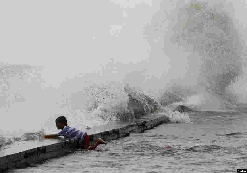 Seorang anak laki-laki berpegangan pada pembatas beton saat ombak besar menghantam pantai Teluk Manila yang dibawa oleh Topan Super Usagi di Navotas City, Metro Manila (21/9).