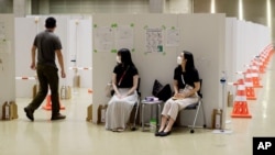 Workers, center, help direct a man into a booth for a coronavirus infection test at the Main Press Center for the 2020 Summer Olympics, July 29, 2021, in Tokyo, Japan. 