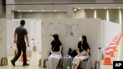 Workers, center, help direct a man into a booth for a coronavirus infection test at the Main Press Center for the 2020 Summer Olympics, July 29, 2021, in Tokyo, Japan. 