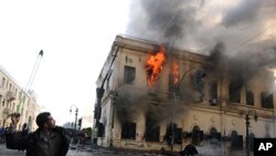 An Egyptian protester uses a slingshot against soldiers, unseen, as a building burns during clashes near Tahrir Square, in Cairo, Egypt, December 17, 2011.