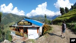 FILE - Trekkers are seen hiking past a rustic guest house near Landruk, Nepal, as clouds shroud the top of Mt. Annapurna South, in a Oct. 21, 2014, photo.