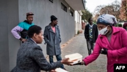 A volunteer for the grassroots charity Hope for Vrededorp reaches out to a woman with a container of home-cooked food, at a daily food distribution in the impoverished district of Vrededorp in Johannesburg, April 28, 2020. 