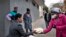 A volunteer for the grassroots charity Hope for Vrededorp reaches out to a woman with a container of home-cooked food, at a daily food distribution in the impoverished district of Vrededorp in Johannesburg, April 28, 2020. 