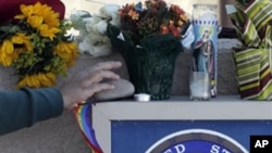 A well-wisher adds an item to a make-shift memorial outside Rep. Gabrielle Giffords' office in Tucson, Ariz., Sunday, Jan. 9, 2011.